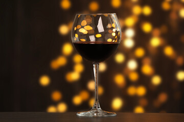 Tasty red wine in glass on table against dark background with blurred lights, bokeh effect