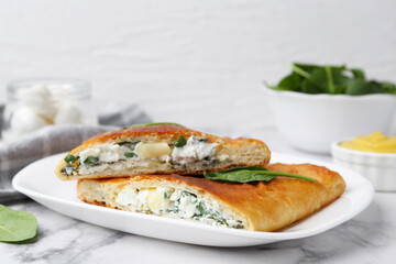 Pieces of tasty calzone with cheese and basil on white marble table, closeup