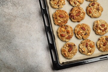 Tasty cookies with nuts in baking tray on gray textured table, top view. Space for text
