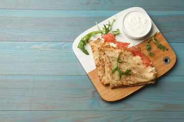 Delicious crepes with salmon, cream cheese and arugula on blue wooden table, top view. Space for text