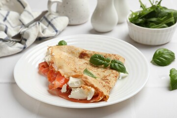 Delicious crepe with salmon, cream cheese and basil on white table, closeup