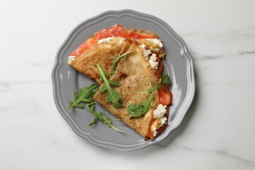 Delicious crepes with salmon, cream cheese and arugula on white marble table, top view