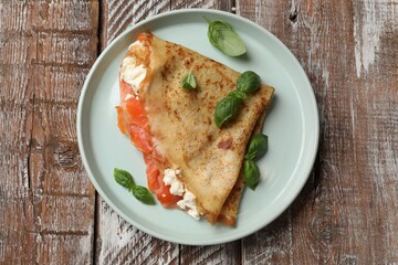 Delicious crepe with salmon, cream cheese and basil on wooden table, top view