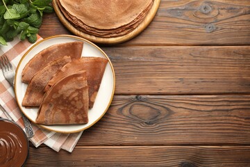 Delicious chocolate crepes, sweet sauce and mint on wooden table, flat lay. Space for text