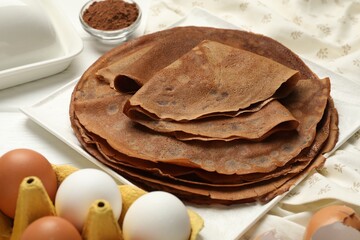 Delicious chocolate crepes and ingredients on white wooden table, closeup