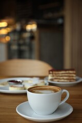 Aromatic coffee and delicious desserts served on wooden table in cafe, closeup