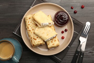 Delicious rolled crepes with cottage cheese, raisins, jam, cranberries and coffee on wooden table, flat lay