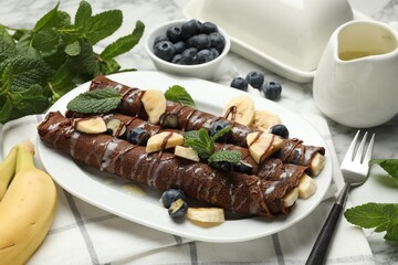 Delicious chocolate crepes with banana and blueberries served on white marble table, closeup