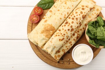 Tasty rolled crepes with cottage cheese and spinach served on white wooden table, top view