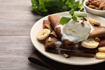 Delicious chocolate crepes with banana, nuts, mint and scoop of ice cream on wooden table, closeup. Space for text