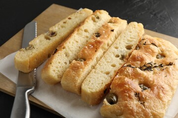 Slices of delicious focaccia bread with olives, thyme, salt and knife on black table, closeup