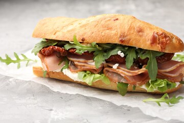 Baguette sandwich with ham and sun dried tomatoes on grey textured table, closeup