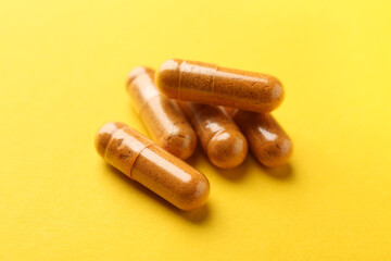 Many turmeric capsules on yellow background, closeup