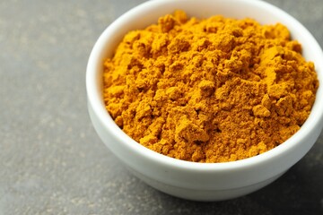 Turmeric powder in bowl on grey table, closeup
