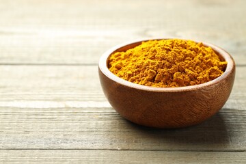 Turmeric powder in bowl on wooden table, closeup. Space for text