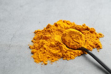 Turmeric powder and spoon on grey table, closeup. Space for text