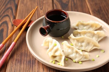 Tasty gyoza (dumpling), soy sauce and chopsticks on wooden table, closeup