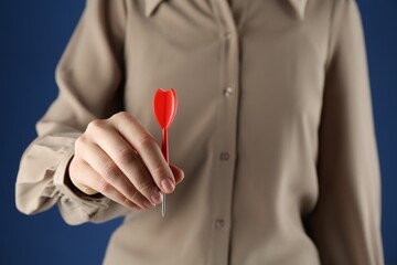 Woman holding dart on blue background, closeup