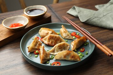 Delicious fried gyoza dumplings with green onions and chili peppers served on wooden table, closeup
