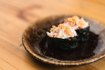 Japanese crab gunkan sushi topped with spicy mayonnaise, served on a rustic ceramic plate on a wooden table.