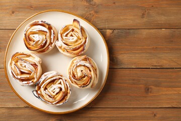 Tasty apple roses with powdered sugar on wooden table, top view. Space for text