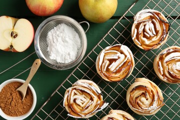 Tasty apple roses with powdered sugar served on green wooden table, flat lay