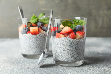 Delicious chia pudding with strawberries, blueberries and mint in glasses on grey table, closeup