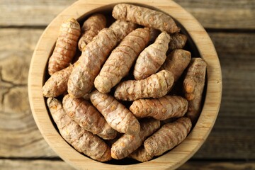 Tumeric rhizomes in bowl on wooden table, top view