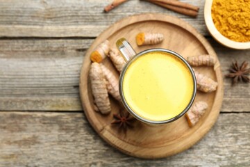 Delicious turmeric latte in glass cup, roots and spices on wooden table, flat lay