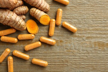 Turmeric capsules in spoon and roots on wooden table, flat lay. Space for text
