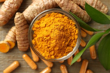Turmeric capsules, powder, roots and green leaves on wooden table, flat lay