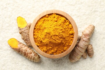 Turmeric powder in bowl and roots on light textured table, flat lay