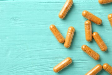 Turmeric capsules on turquoise wooden table, flat lay. Space for text
