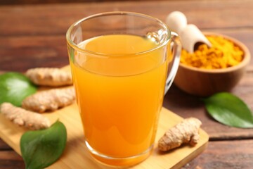Aromatic turmeric tea in glass mug, roots, powder and green leaves on wooden table, closeup