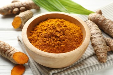 Aromatic turmeric powder, fresh roots and leaves on white wooden table, closeup