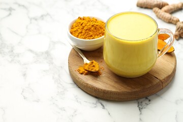 Delicious turmeric latte, powder and rhizomes on white marble table, closeup. Space for text