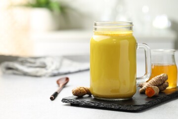 Delicious turmeric latte with honey and rhizomes on grey table, closeup. Space for text