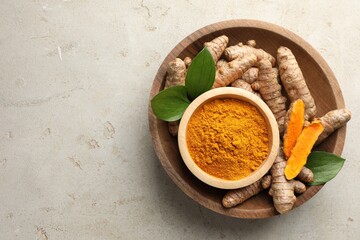 Aromatic turmeric powder in bowl, fresh roots and leaves on light grey table, top view. Space for text
