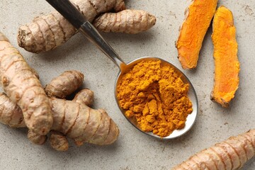 Aromatic turmeric powder in spoon and fresh roots on light grey table, flat lay