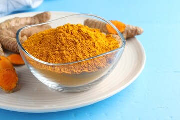 Aromatic turmeric powder in bowl and fresh roots on light blue wooden table, closeup