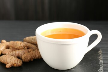 Aromatic turmeric tea and rhizomes on black table, closeup