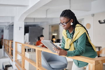 Young woman using digital tablet in contemporary office space with colleagues in background, focusing on task and creating a collaborative environment