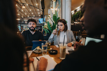 Diverse group of professionals discussing work and collaborating during a meeting at a cozy cafe with a modern interior and natural lighting, creating a dynamic and productive atmosphere for teamwork.