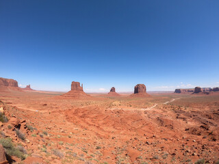 A sweeping view of Monument Valley, showcasing red rock mesas under a vast blue sky, blending Arizona and Utah’s rugged beauty.