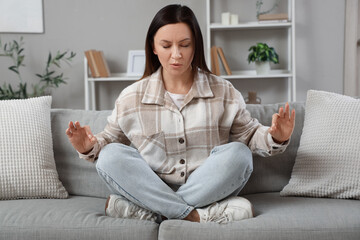 Worried woman meditating and trying to calm down while sitting on sofa at home