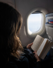 Young woman reading a book in an airplane besides the window. stock photo