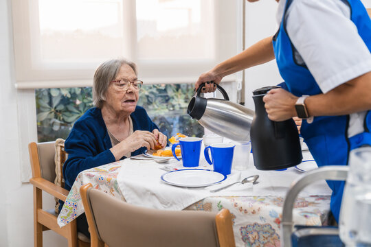 Caregiver serving breakfast to elderly woman in nursing home - Powered by Adobe