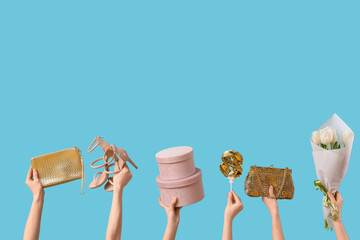 Female hands holding flowers with gift boxes, handbags and shoes on blue background. Shopping for...