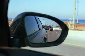 Rearview mirror reflection of a coastal road with cars