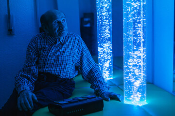 Elderly man relaxing in sensory room with bubble tubes